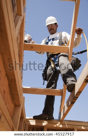 Construction worker on the roof of a house under construction, with a clear blue sky in the background. Horizontal format.