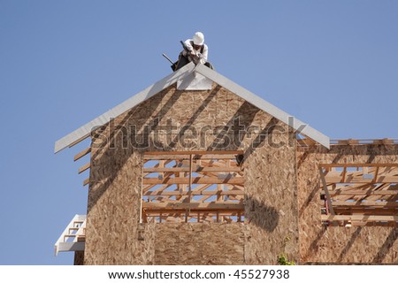 Construction worker on the roof of a house under construction, with a clear blue sky in the background. Horizontal format.