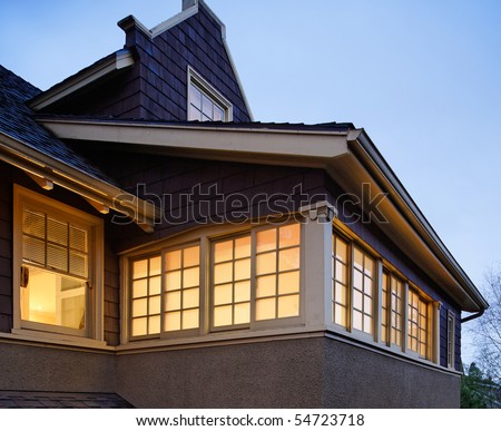 Low angle view of the upper floors of a large house. The windows are illuminated with interior lighting. Square shot.