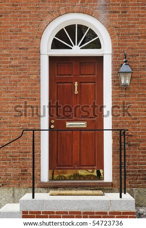 An elegant red door with brass accents in a brick building. Vertical shot.