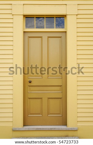 An unadorned yellow door set in to the facade of a wooden building. Vertical shot.