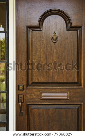 The wooden front door of a home with glass panel to the side. The glass is reflecting the homes opposite the door. Vertical shot.
