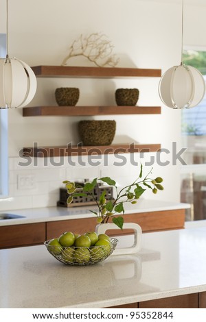 A modern kitchen shown with solid counter tops and wood shelving.