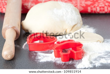 Baking biscuits at home with colourful red cookie cutters on a floured surface in front of a mound of fresh dough