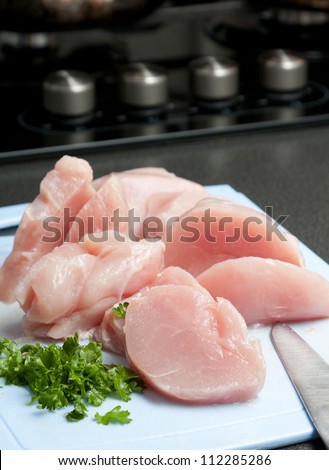 Diced healthy lean white meat chicken pieces on a chopping board with fresh herbs ready to be used in the preparation of the evening meal