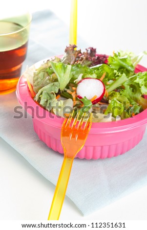 Fresh leafy green salad in a pink bowl with plastic disposable cutlery