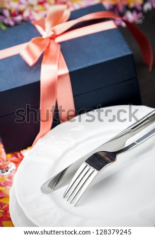 Simple stylish white dinner plates and cutlery with a gift box tied with a decorative red bow, high angle closeup shot