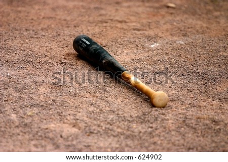 A wooden baseball bat dropped in the dirt.