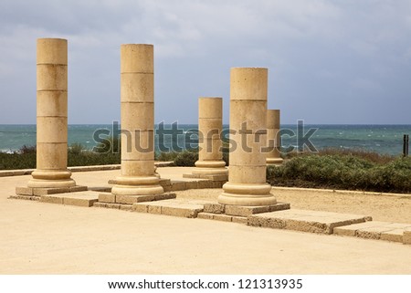 A set of stone pillars standing near the coast at the ancient Roman city of Caesaria in Israel. The stones glow against the gloomy skies in the background.
