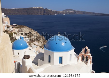 Classic view of blue-painted domes on Orthodox Greek churches in the town of Oia on the island of Santorini in the Greek Islands. The town of Thera is in along the island rim in the background.