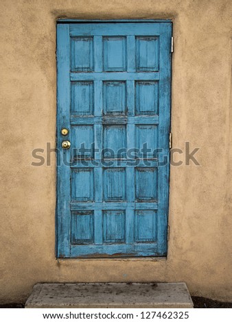 An old blue door in a adobe mud wall portrays an element of decay with layers and layers of peeling paint and cracks.