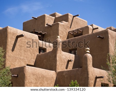 The facade of a hotel built to look like an old native American pueblo with adobe walls, square corners, exposed beams, and more.