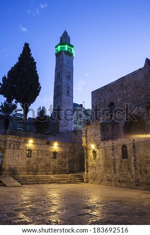 Illuminated by a green neon light at night, a minaret stands next to the courtyard in front of the Church of the Holy Sepulchre in the Old City of Jerusalem.