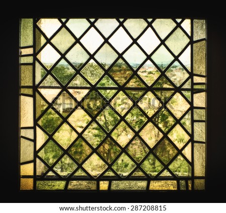 An old stained glass window with pigmented window panes and leaded glass distorts the French countryside into a a view that looks like an impressionist painting.