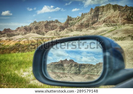 A mountain range of the colored hills as viewed through the rear-view mirror window of a car by the roadside in Badlands National Park in South Dakota.