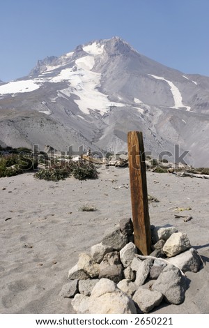 A wood post marking a hiking trail with the summit of Mt. Hood in the background. This area of Mt. Hood is composed of loose volcanic ash and sand.