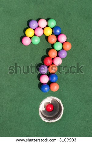 A number of gaily colored golf balls formed into the shape of a question mark, using the silver cup as the period marker.