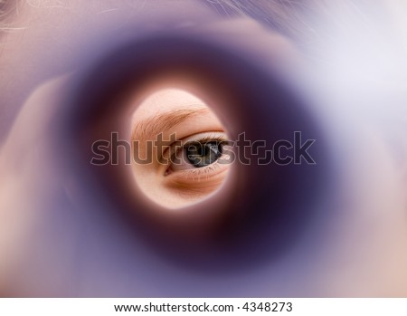 A girl\'s eye staring through the center of a piece of paper that has been rolled into a tube like a periscope. The close focus has made this more abstract.