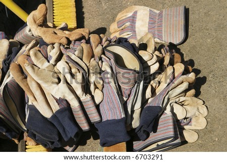 Leather work gloves left in a large pile on the ground after a large work party had used them to move gravel and dirt.