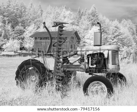 An old tractor on a farm with a barn in the background. In black and white infrared.