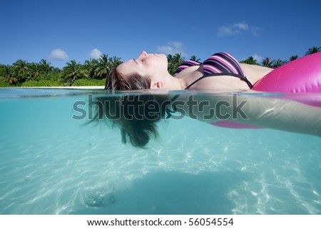 Young woman in a bikini relaxing upon a floating tire within the indian ocean