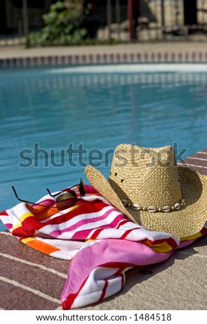 Hat, glasses and a beach towel by a pool