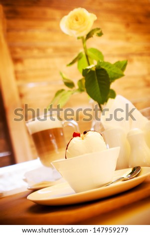 Sweet cream, coffee latte and flower rose on the warm wooden background
