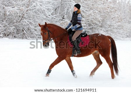 Young woman riding horse through a snowy park