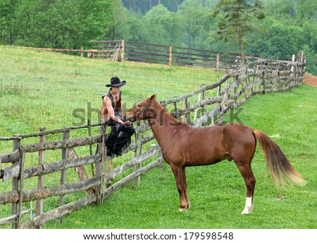 Man in cowboy clothes sitting on the fence beside the horse