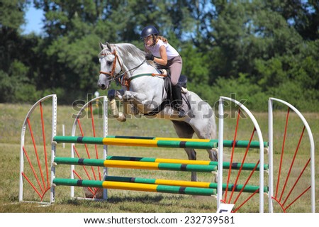 Girl racing horse over jump on course