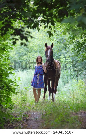 Young beautiful woman walking with a horse in the forest bush