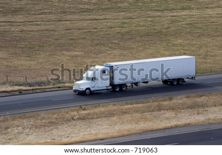A tractor-trailer truck in cruising along the highway.