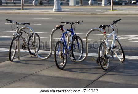 Three bikes are locked to a modern looking sidewalk rack.  The brand names and logos have been removed from all parts of the bikes.