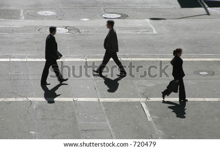 Three business people pass in the cross walk.