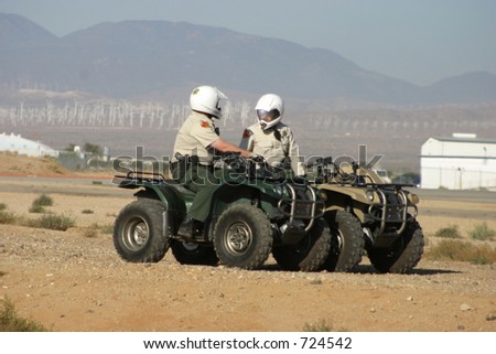 A couple cops patrol a desert airport on their ATV\'s.