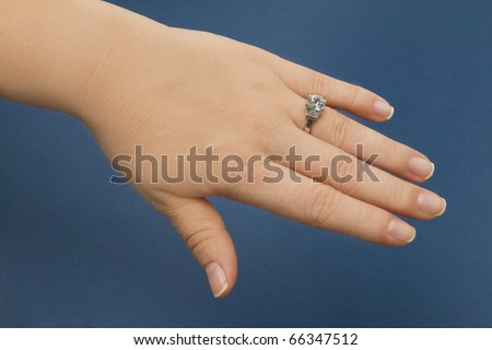 Female hand over blue background wearing a diamond engagement ring with white gold body.