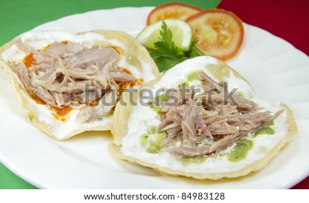 Pork Tostadas mexican dish made with fried tortilla, pork meat and seasoned with sour cream, shredded cheese and hot green or red sauce.