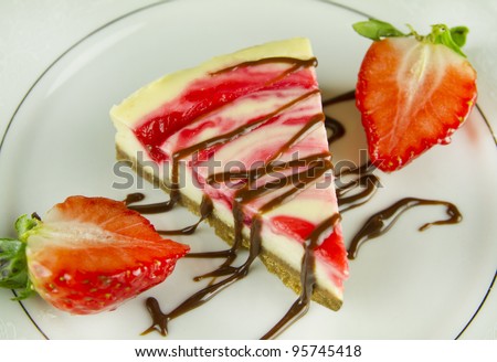 Strawberry Cheesecake. Traditional Strawberry cheesecake adorned with liquid chocolate and half sliced strawberries.