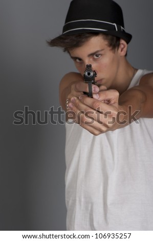 A young man with a gun in his hand on a gray background in the studio