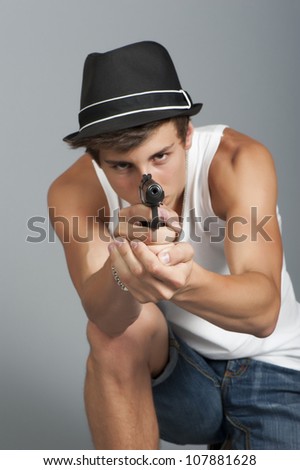 A young man with a gun in his hand on a gray background in the studio, focus on the hands with a gun