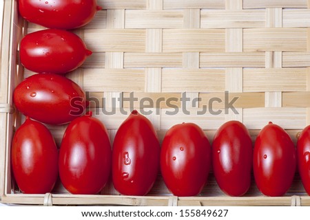 Small oblong red ripe tomatoes on a wicker wooden platter