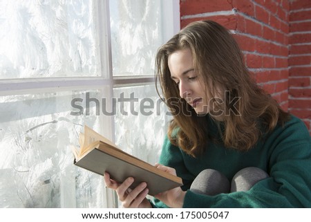 A young woman with a book by the winter window