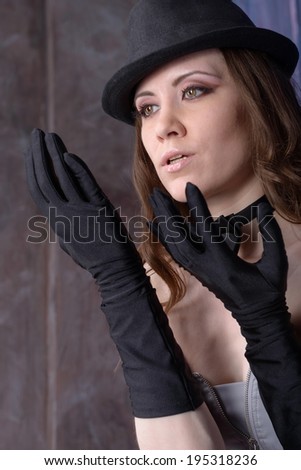 Beautiful young woman in a black hat and gloves on purple background