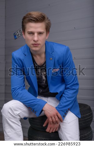 Young man in a blue jacket sitting on tires in the car garage