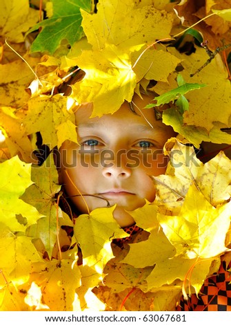 Face of child in leaves in autumn