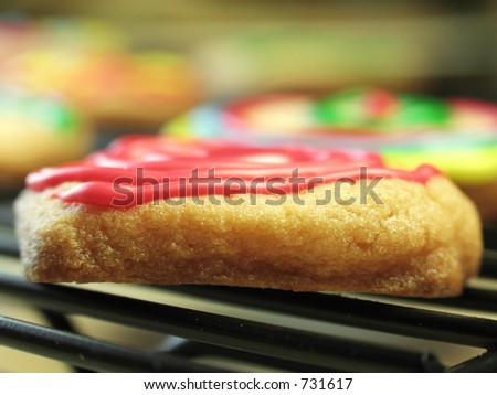 A closeup of a red frosted sugar cookie cooling on a baking rack, with very shallow focus.