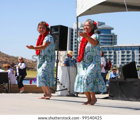 TEMPE, AZ - MARCH 31: Two unidentified women, wear print dress and lei, while they dance to HawIiaan music at the Dragon Boat Festival at Tempe Town Lake, March 31, 2012.