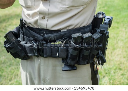 Police officers heavy tactical belt holds an array of tools: a pistol, electric Taser, ammo clips, radio, knife, car keys and radio.