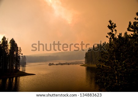 Smoke from a woodland wildfire obscures the sky and sun along the shore of Lake Yellowstone.