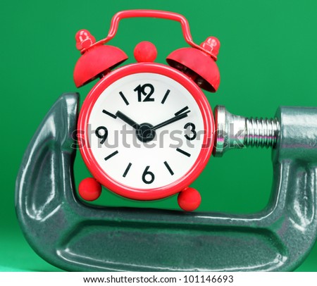 A red colored  alarm clock placed in a Grey clamp against a pastel green background, asking the question do you manage your time effectively.